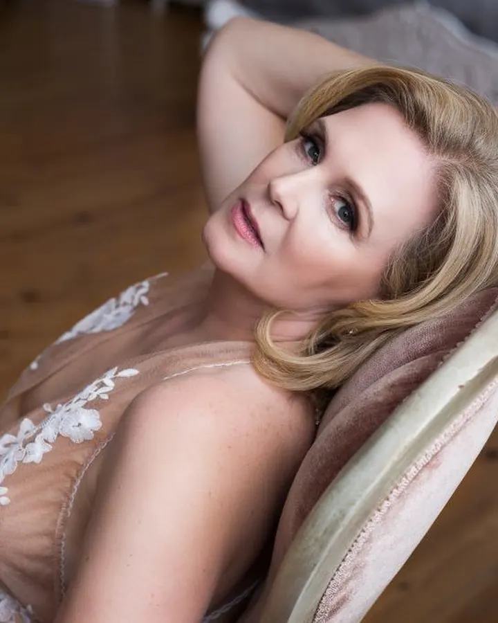 Femme blonde en body noir, allongée sur un lit, vue de dos