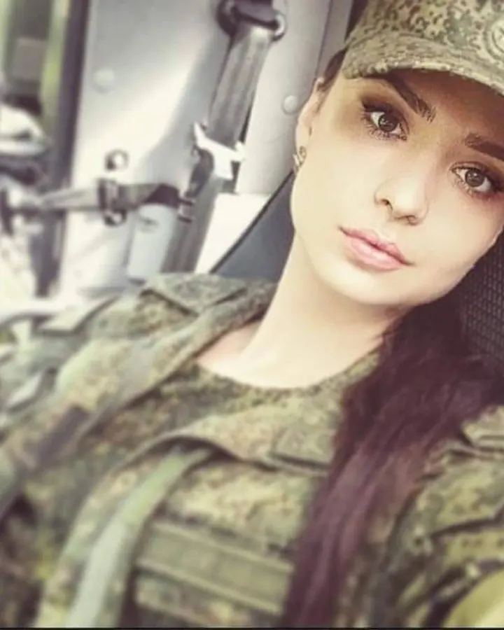 Femme aux cheveux châtains en tenue militaire camouflage, assise dans un véhicule, regardant l'appareil.