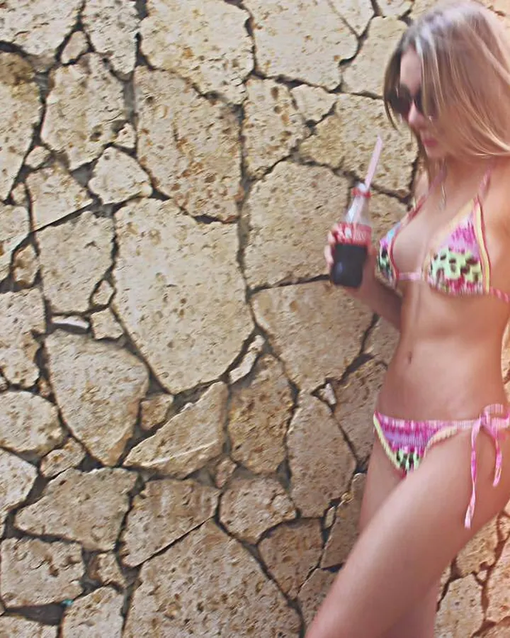 Jeune femme blonde en maillot de bain coloré, Coca à la main, mur de pierre en arrière-plan