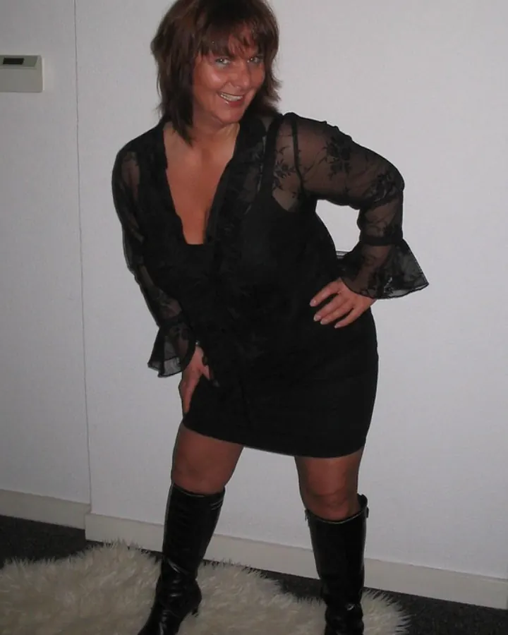 Femme en tenue noire, posant sur un lit, avec un cadre décoratif au mur.