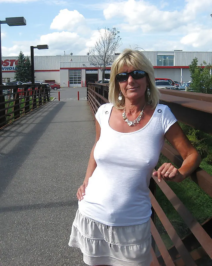 Femme européenne aux cheveux platine portant un haut blanc et une jupe blanche, posant sur un pont ensoleillé