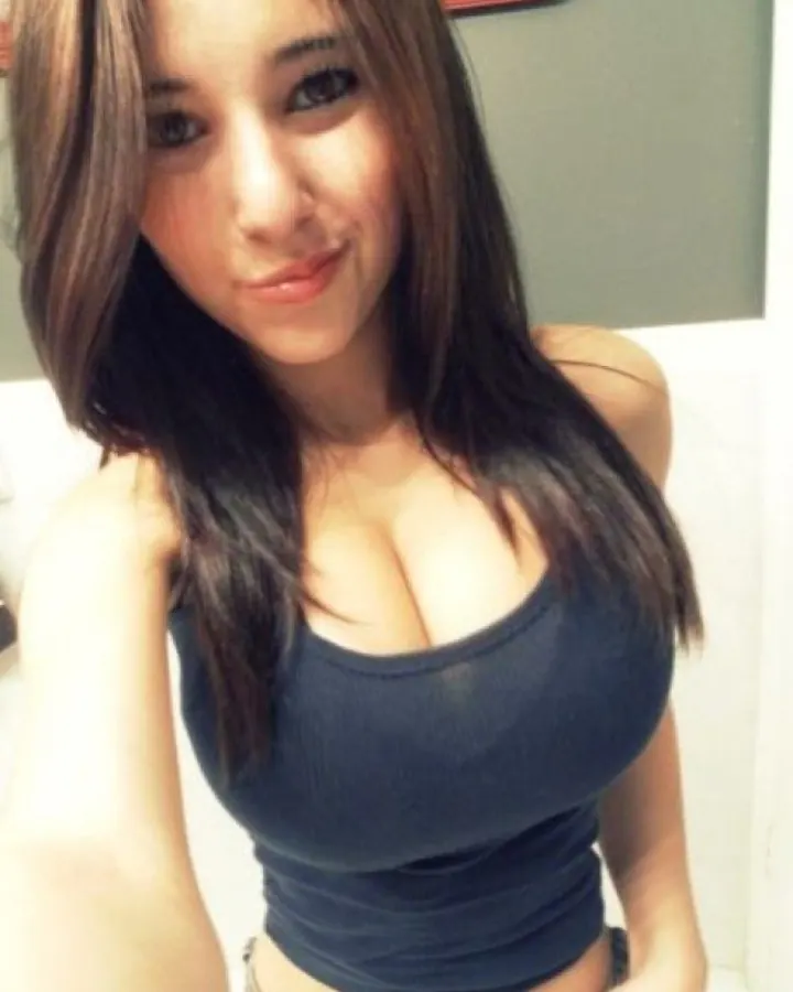 Jeune femme aux cheveux châtains portant un haut bleu foncé ajusté, posant près d'un mur gris avec une expression légèrement souriante.