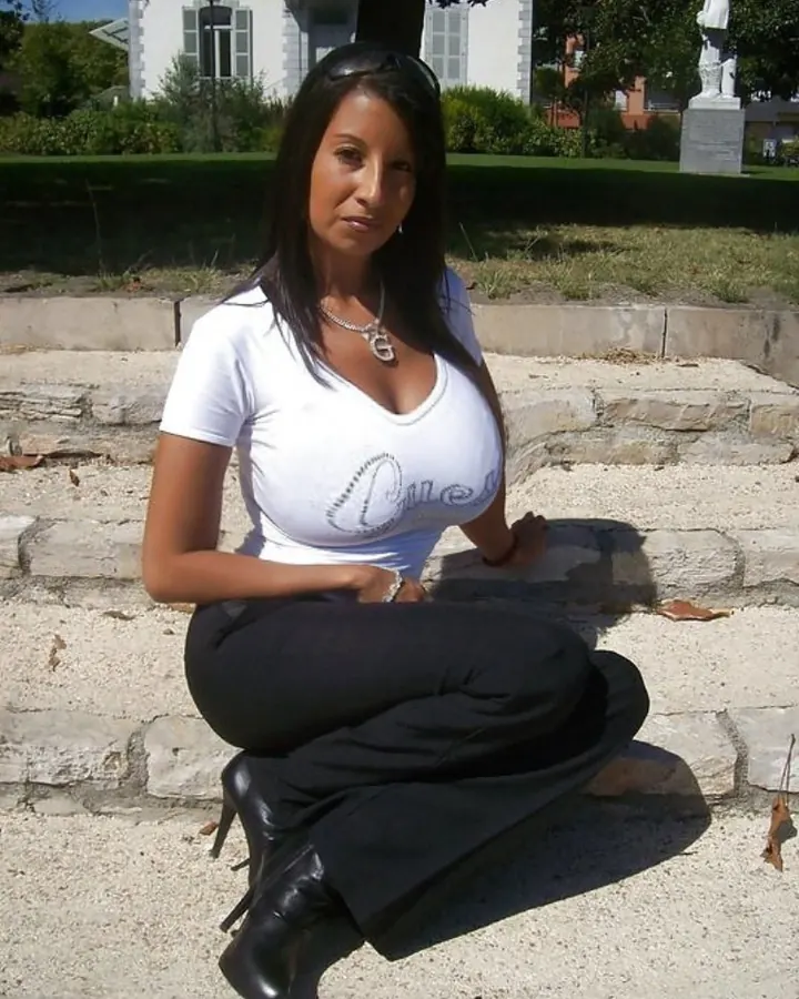 Femme en haut noir, assise sur un canapé, regardant vers la caméra, main sur la hanche.