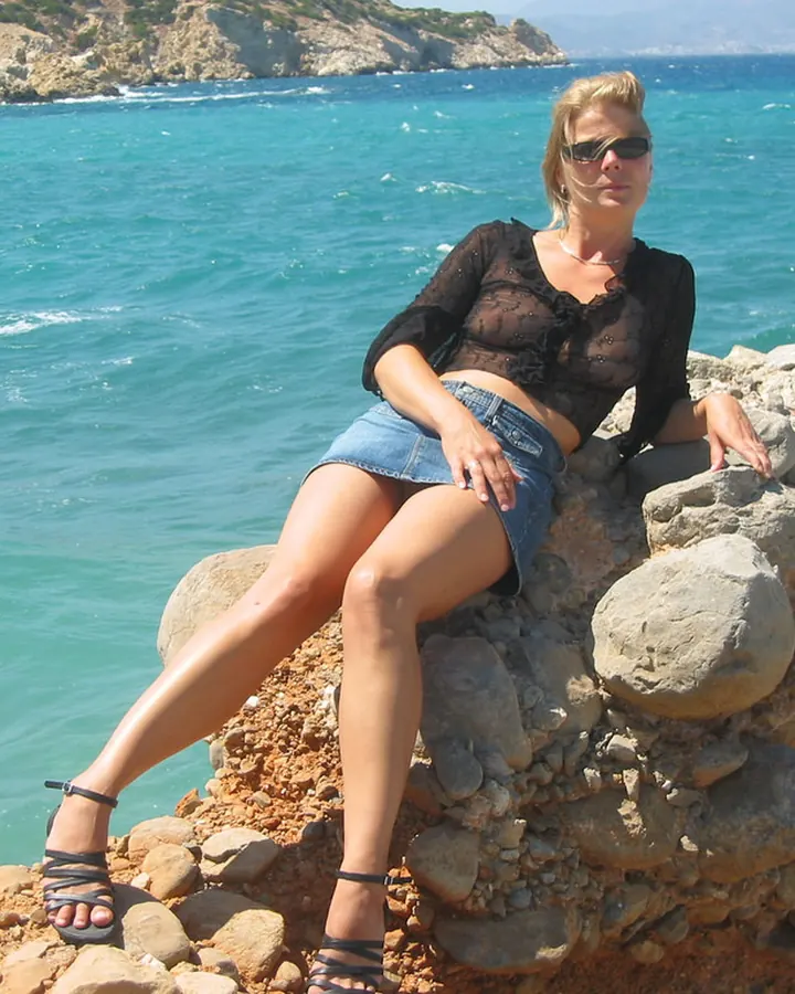 Femme blonde en maillot de bain noir, assise sur un rocher près de la mer