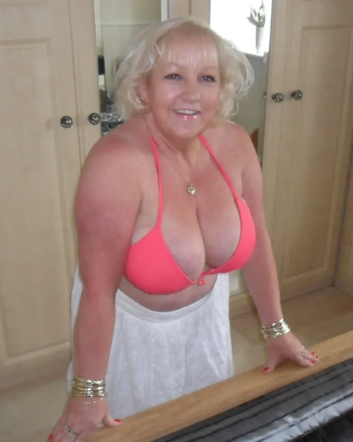 Femme en bikini rose, cheveux blancs, souriant dans une chambre