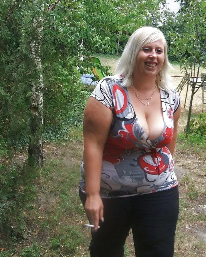 Femme blonde en robe rouge, debout près d'une porte en bois, collants noirs et chaussures rouges.