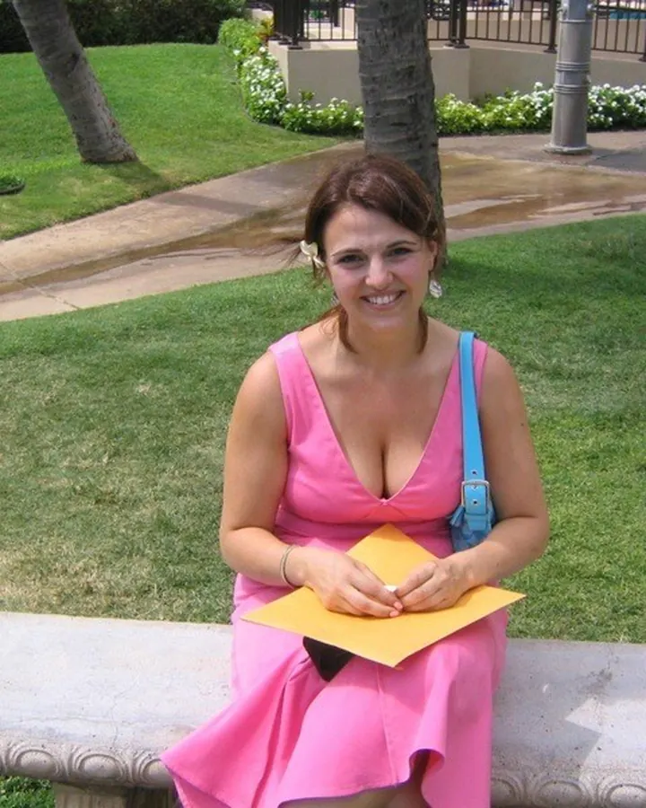 Femme souriante, vêtue d'une robe rose fluo, assise sur un banc en plein air, tenant une feuille jaune.