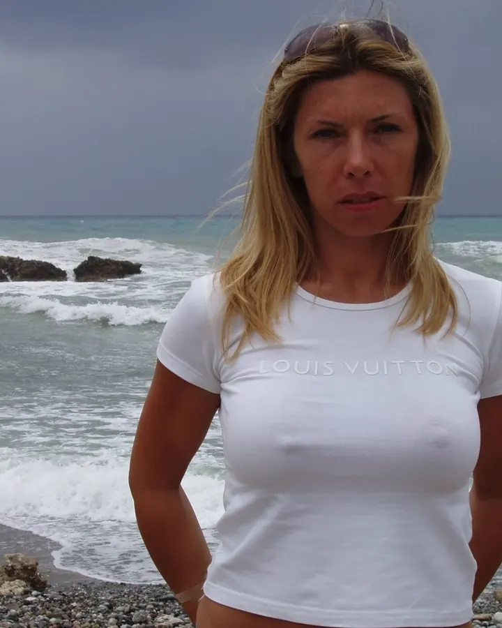 Femme blonde en t-shirt blanc, regard vers l’appareil, cheveux dans le vent.