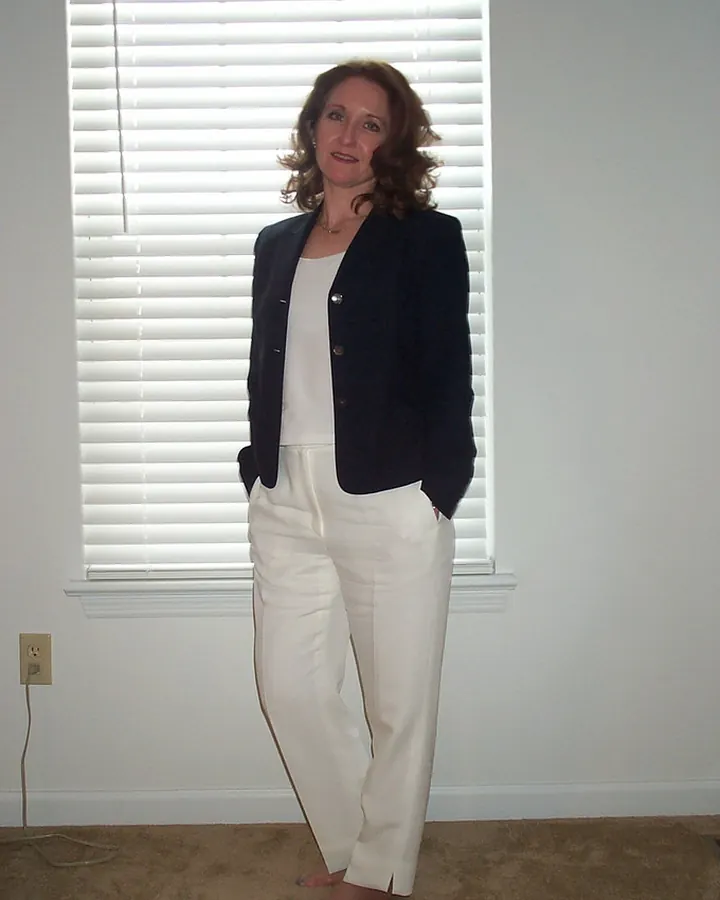 Femme aux cheveux bruns, en robe noire et collants, allongée sur un canapé en cuir.