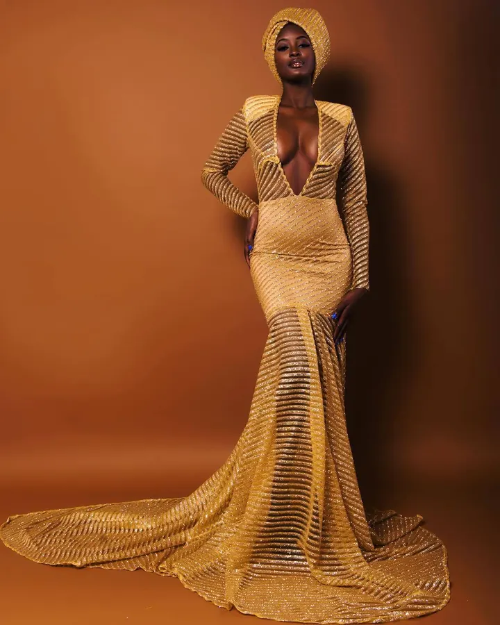 Femme noire en lingerie dorée à dentelle, allongée sur le côté, le ventre exposé, dans une lumière douce et tamisée.