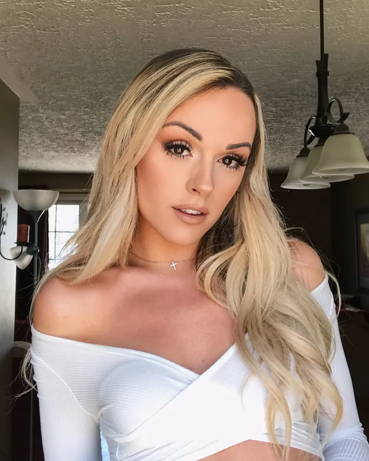 Femme blonde en bikini blanc, posant près d'une piscine, regardant l'appareil photo avec un sourire discret