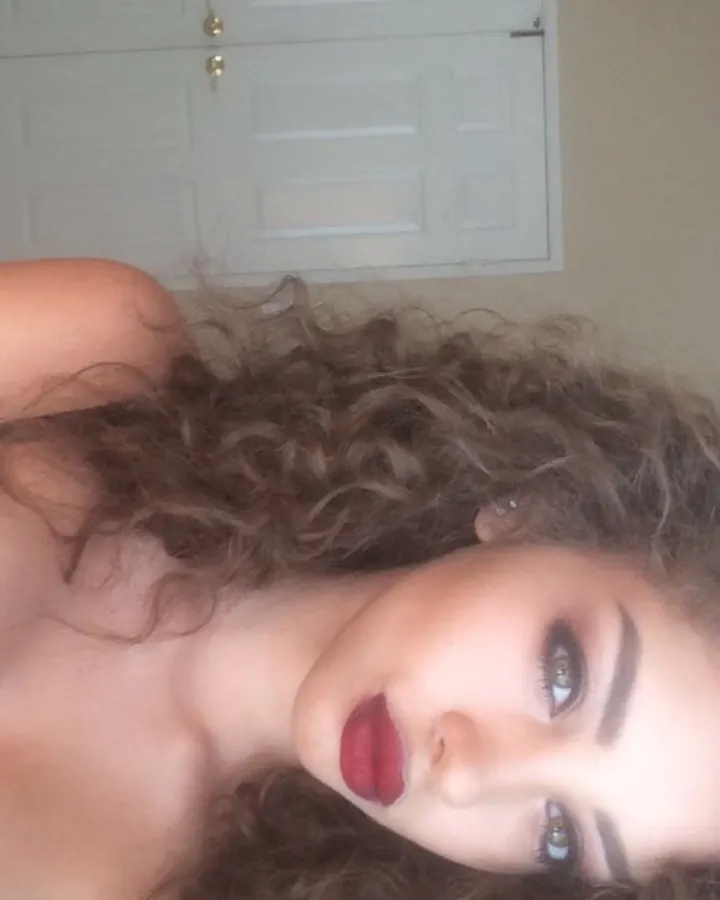 Femme aux cheveux bruns, en collants noirs et culotte de couleur, prenant un selfie dans un miroir avec flash.
