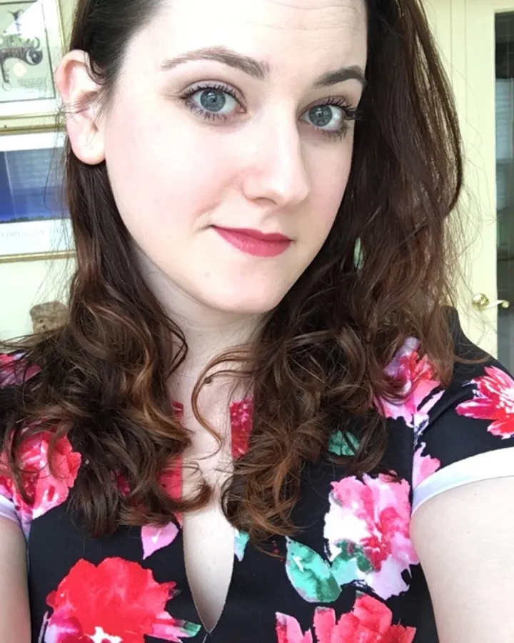 Femme aux cheveux bruns, portant un haut noir, prenant un selfie dans une chambre avec des guirlandes lumineuses.