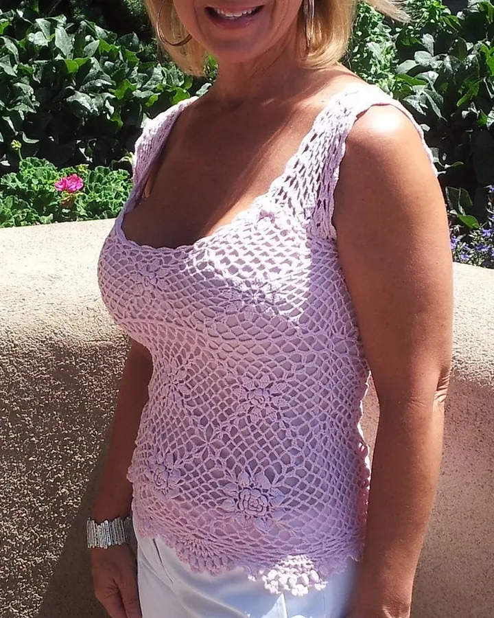 Femme blonde souriante, portant une robe blanche avec ceinture marron, debout dans un jardin ensoleillé.