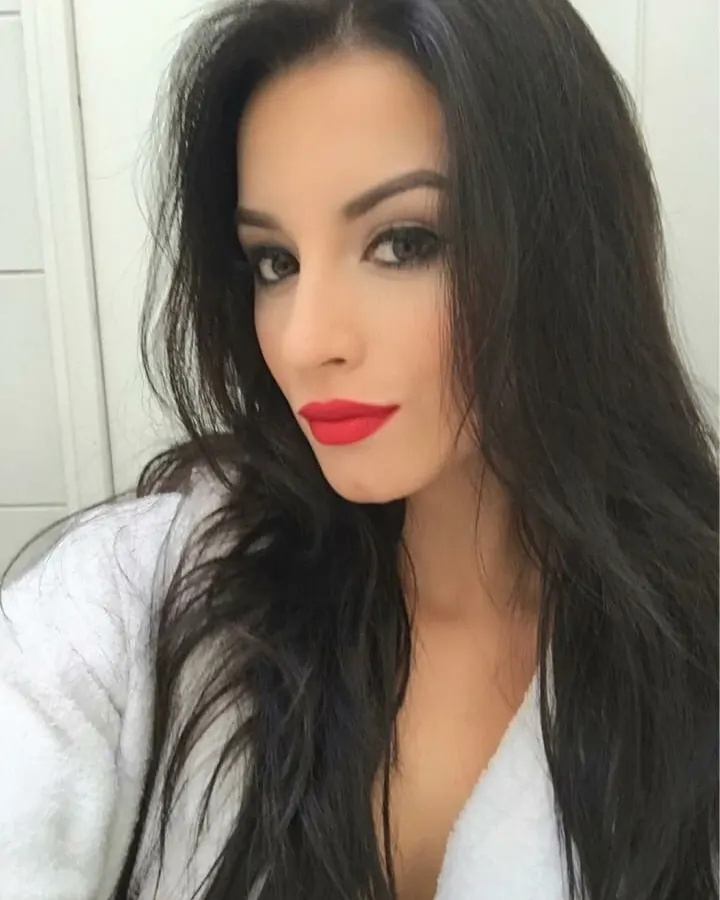 Femme aux cheveux noirs, regardant directement l'appareil photo, portant un peignoir blanc, avec du rouge à lèvres vif.