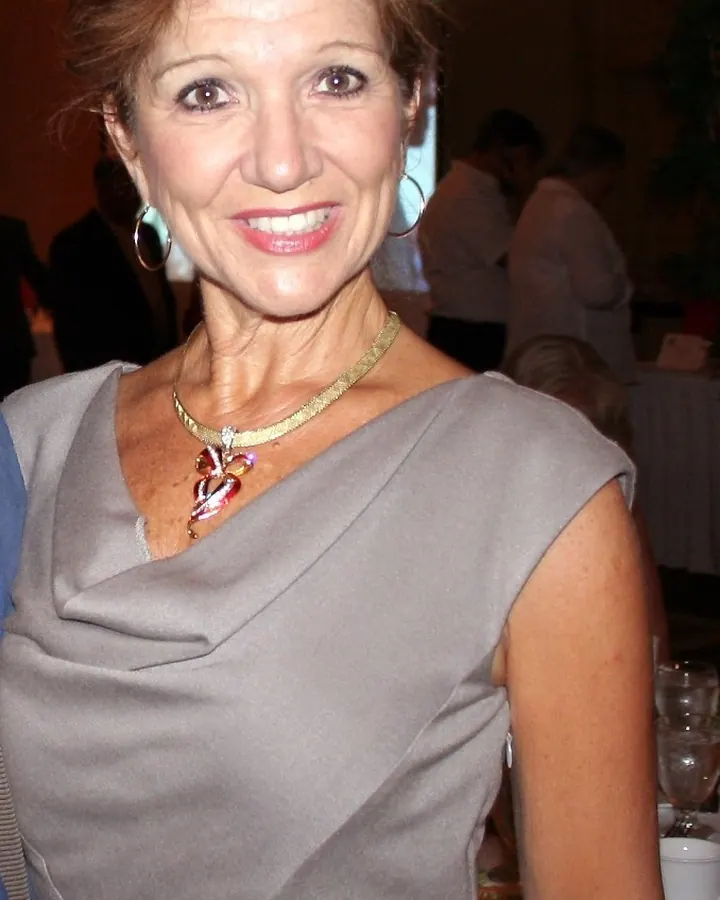 Femme aux cheveux châtains portant une robe grise avec un col drapé, souriant à la caméra lors d'un événement social.